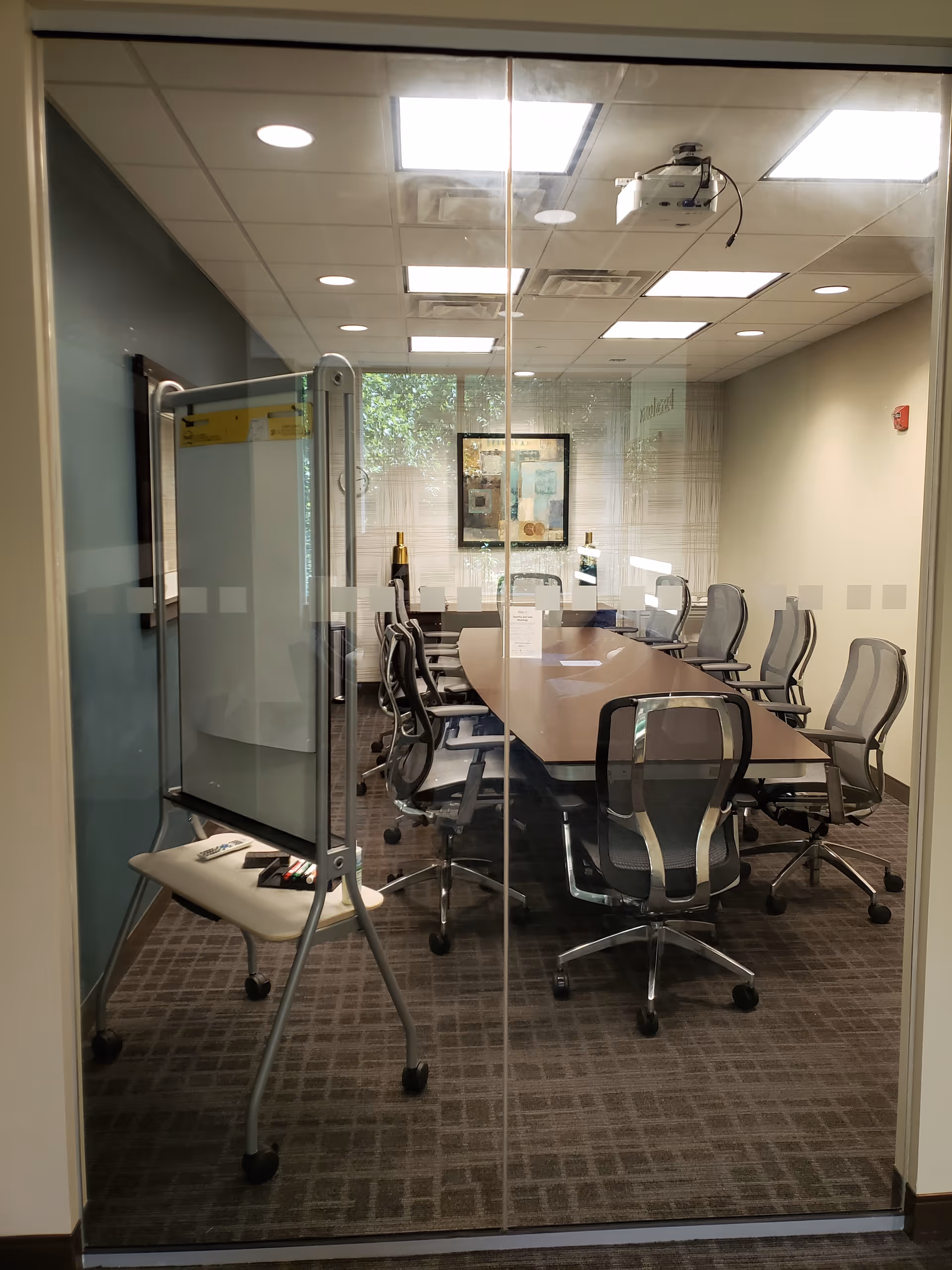 Glass-walled conference room with a long table, chairs, and a projector.