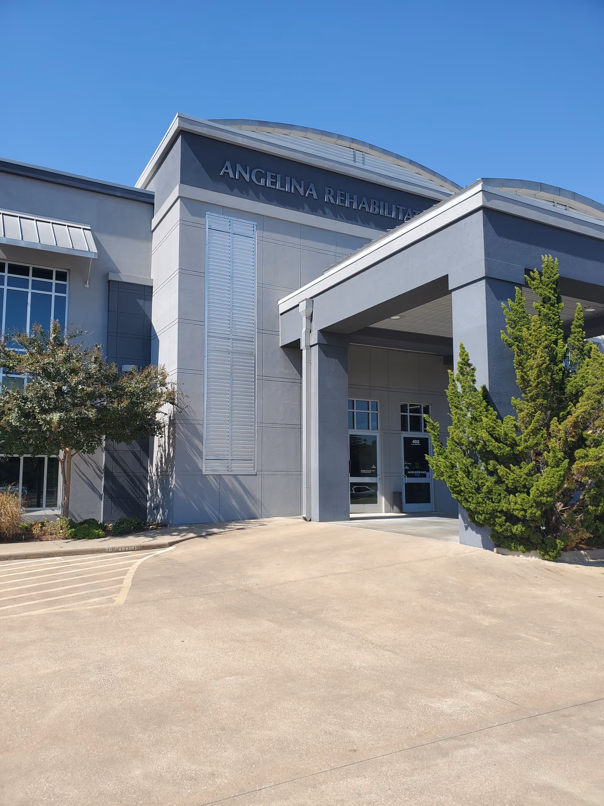 Exterior view of Angelina Rehabilitation entrance with driveway, trees, and blue sky