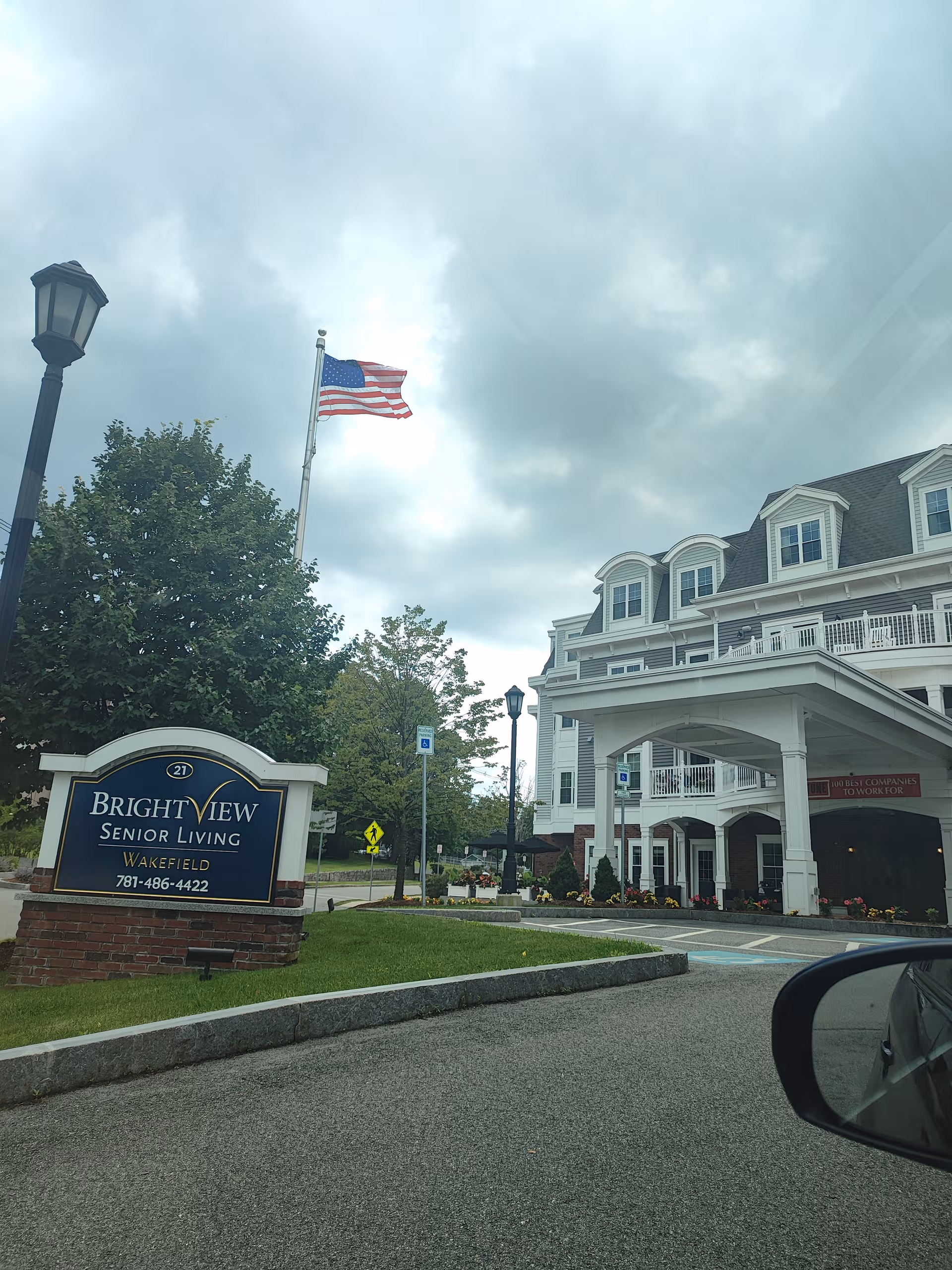 Exterior view of BrightView Senior Living Wakefield with sign, flag, and white multi-story building.