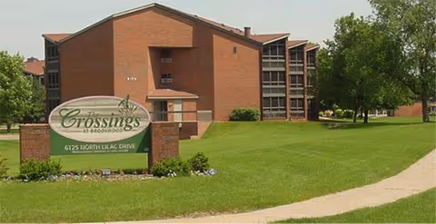 Brick building with manicured lawns and a 'The Crossings at Brookwood' sign in front.