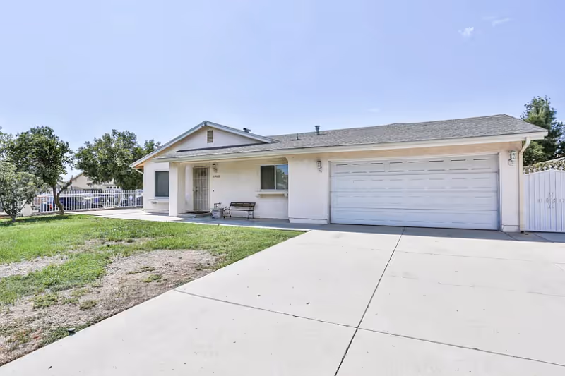 Single-story light-colored house with an attached two-car garage, front lawn, and concrete driveway.
