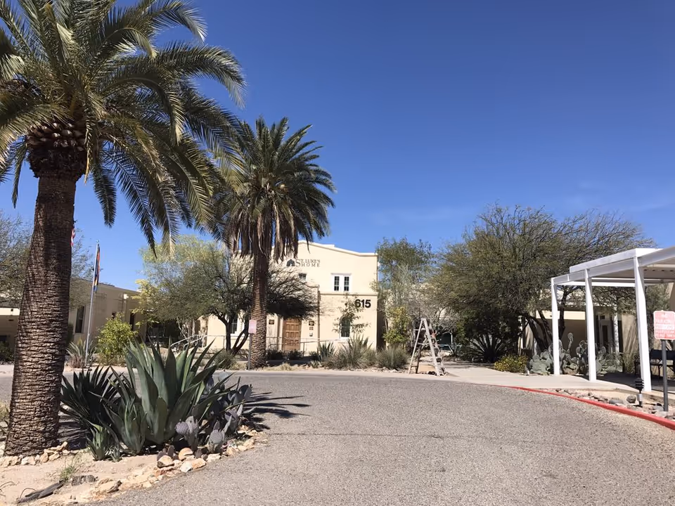 Front entrance of St. Luke's Home building with palm trees, desert landscaping, and a circular driveway under a clear blue sky.