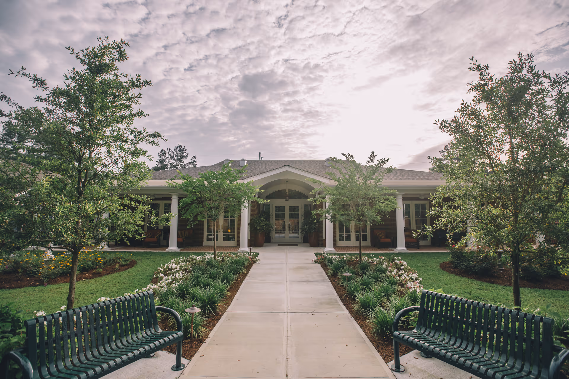 Symmetrical building entrance framed by trees, benches, and manicured landscaping.