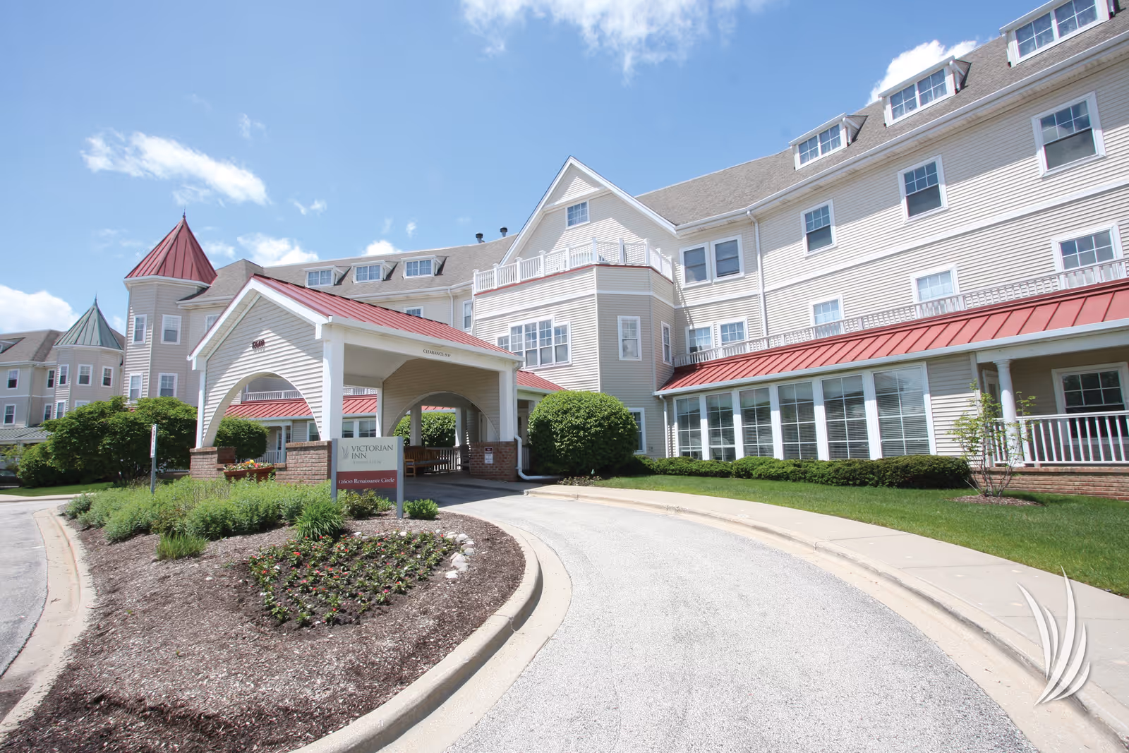 Senior living facility exterior with beige siding, red roof, and arched entrance.