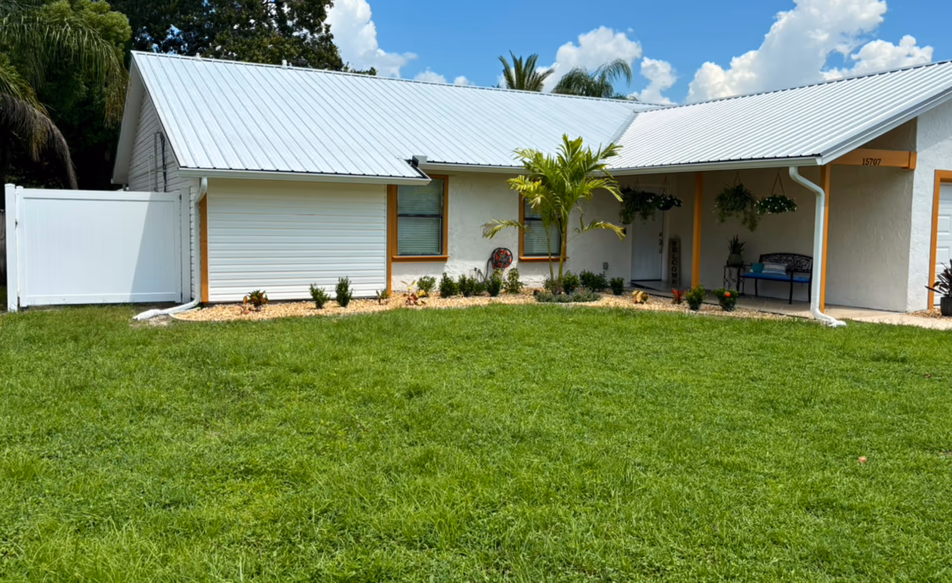 A single-story senior living facility exterior with a manicured lawn, palm tree, and porch.
