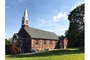 Brick retirement community building with a tall church-style steeple and manicured lawn.