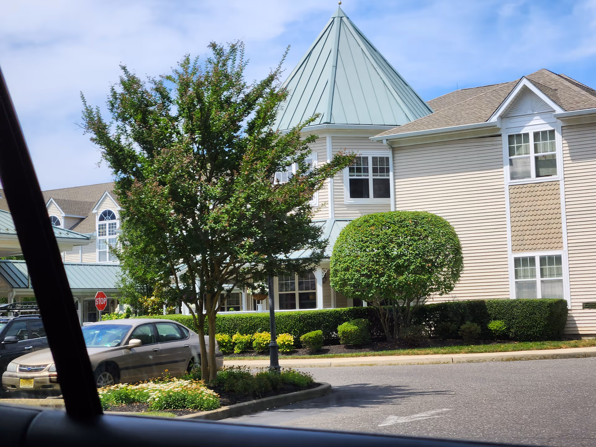 Exterior view of a senior living building with trees and parked cars.