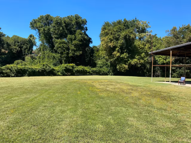 Expansive grassy yard with trees and a covered outdoor seating area on the right.