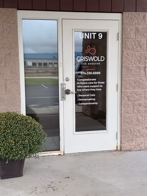 Glass door labeled UNIT 9 with Griswold branding, outside beige brick building, and a plant nearby.