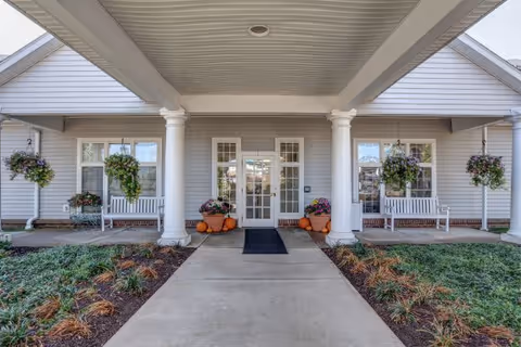 Front entrance to a senior living facility with columns, hanging baskets, and pumpkins.