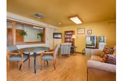Cozy senior living common area with dining table, sofas, and bookshelf.