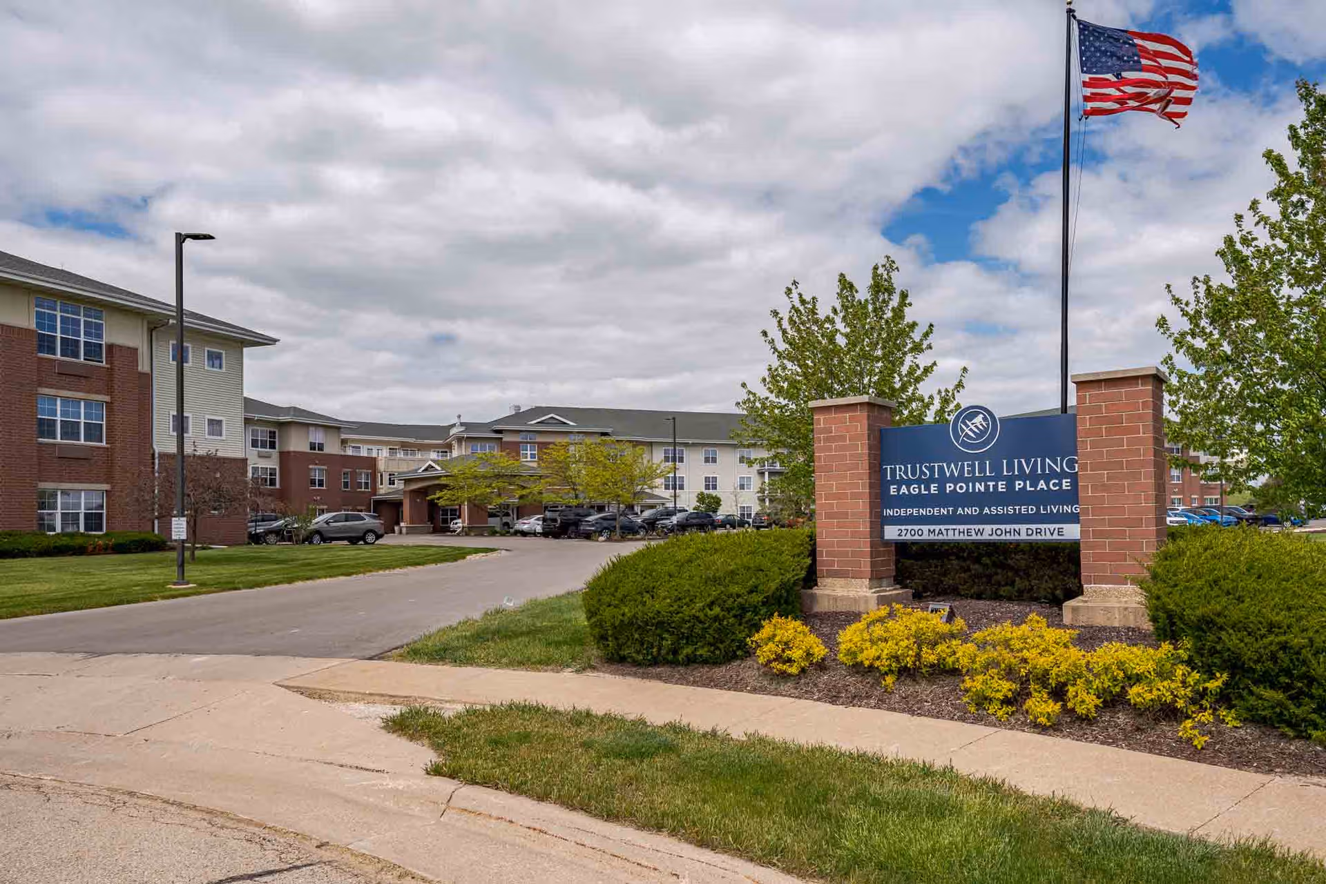Exterior view of Trustwell Living at Eagle Pointe Place with sign, flag, and campus buildings.