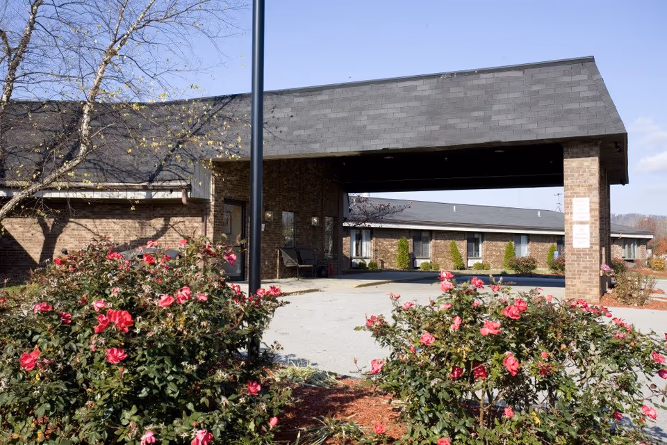 Brick senior living facility entrance with a covered drive and blooming rose bushes.