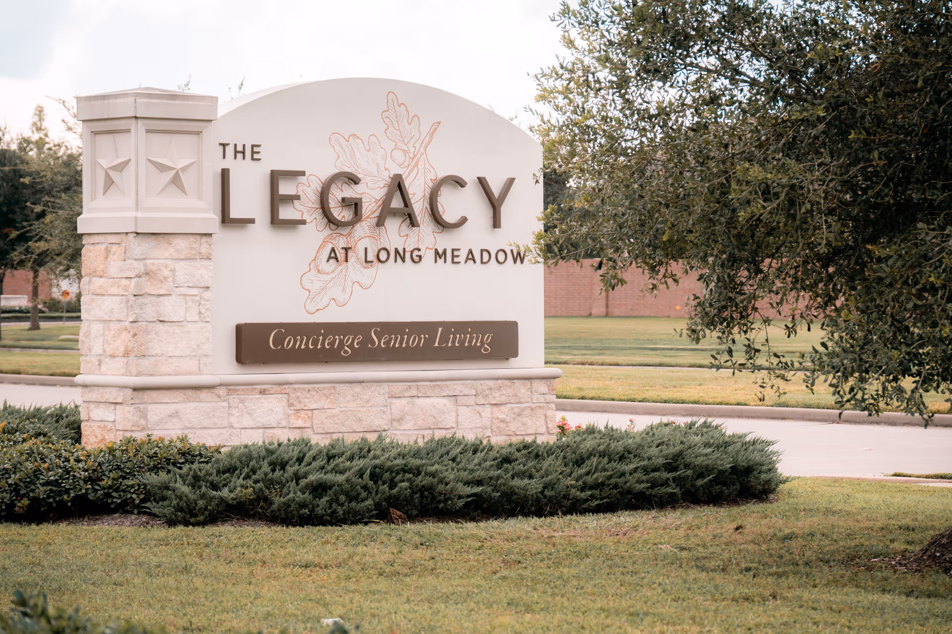 Stone entrance sign reading "The Legacy at Long Meadow — Concierge Senior Living" set in landscaped lawn.