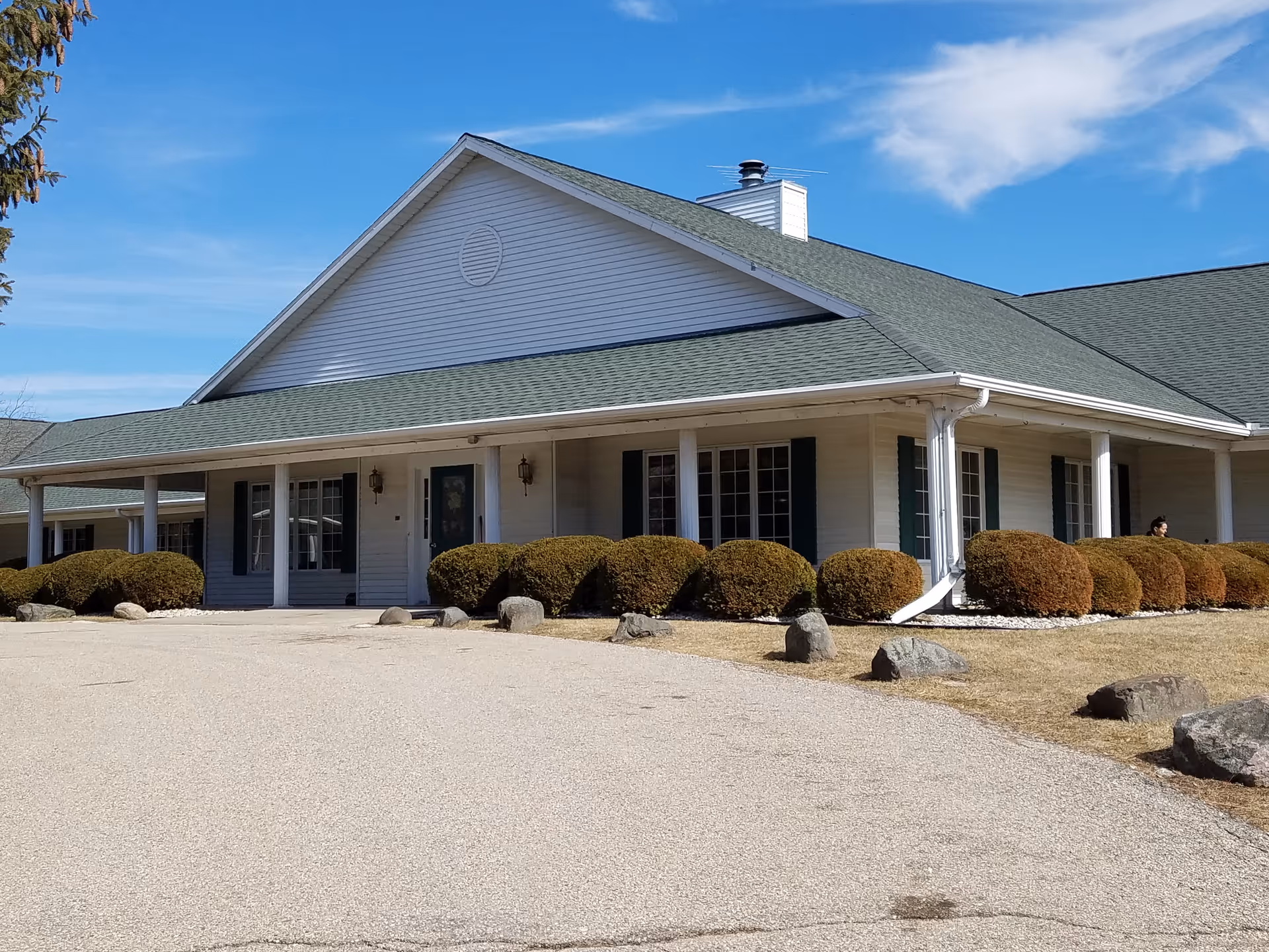 White, single-story senior living facility with green roof and neatly trimmed shrubs.