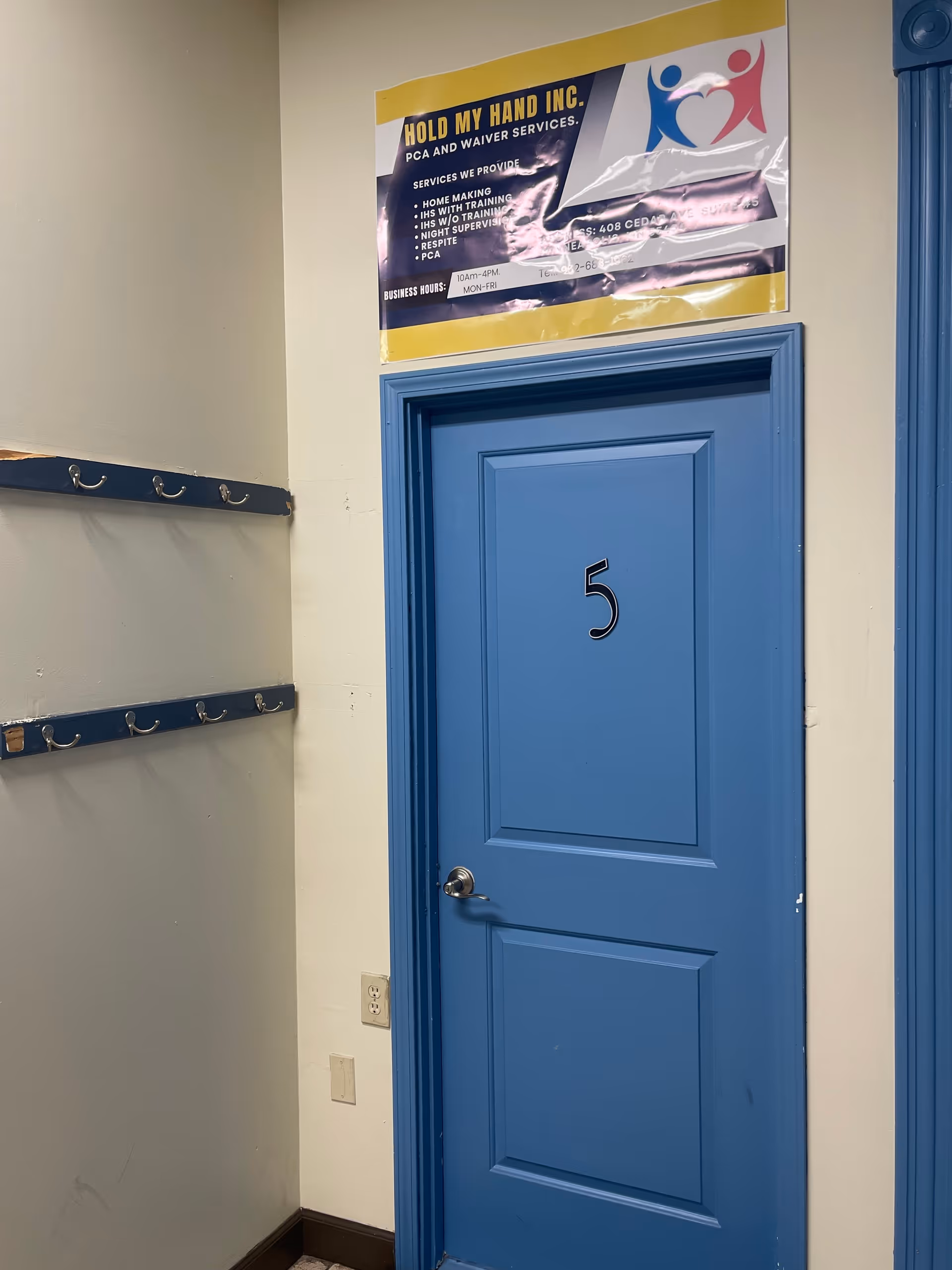 Blue numbered door 5 in a hallway with coat hooks and a poster overhead.