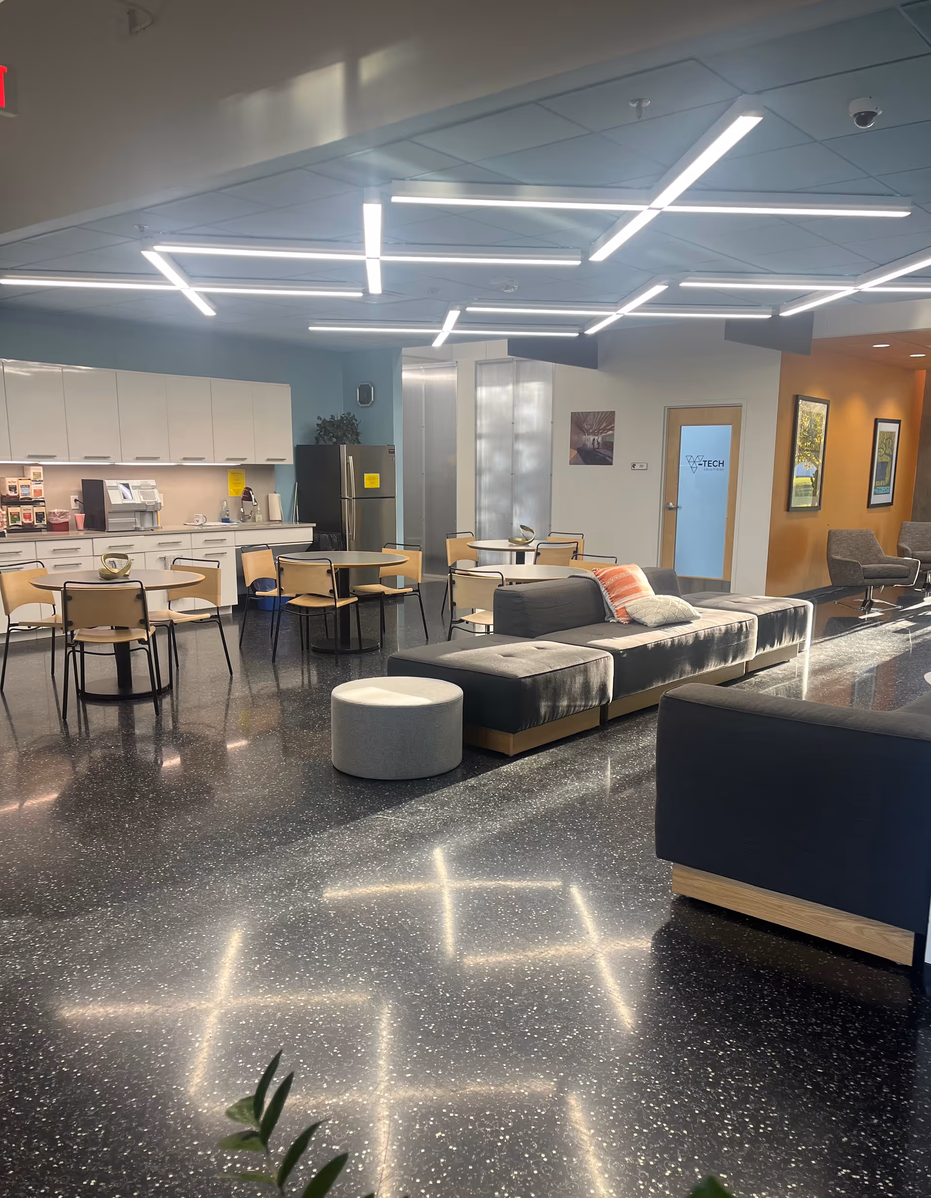 Modern senior living lounge with modular seating, tables, and a kitchen area.