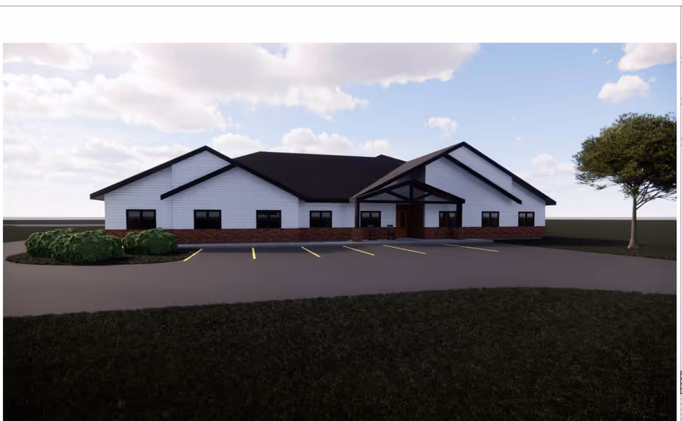 A single-story white senior living facility exterior with brick base and parking lot.