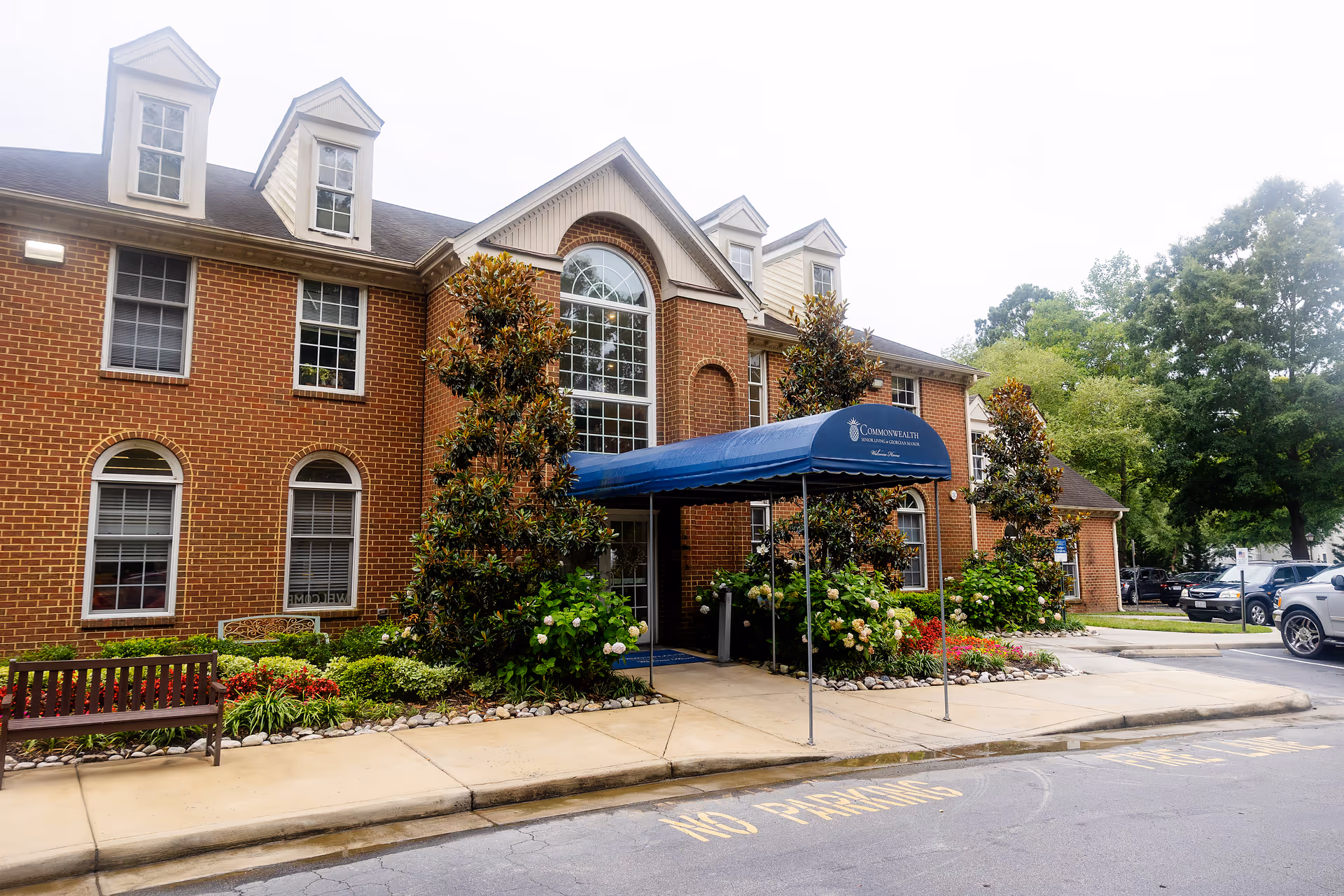 Brick senior living building with a blue entrance canopy and landscaped front garden.