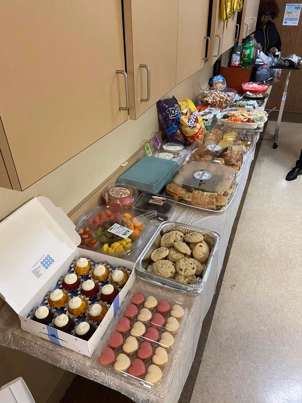 Long serving table with assorted snacks, pastries, fruit, and cupcakes in a senior living facility.