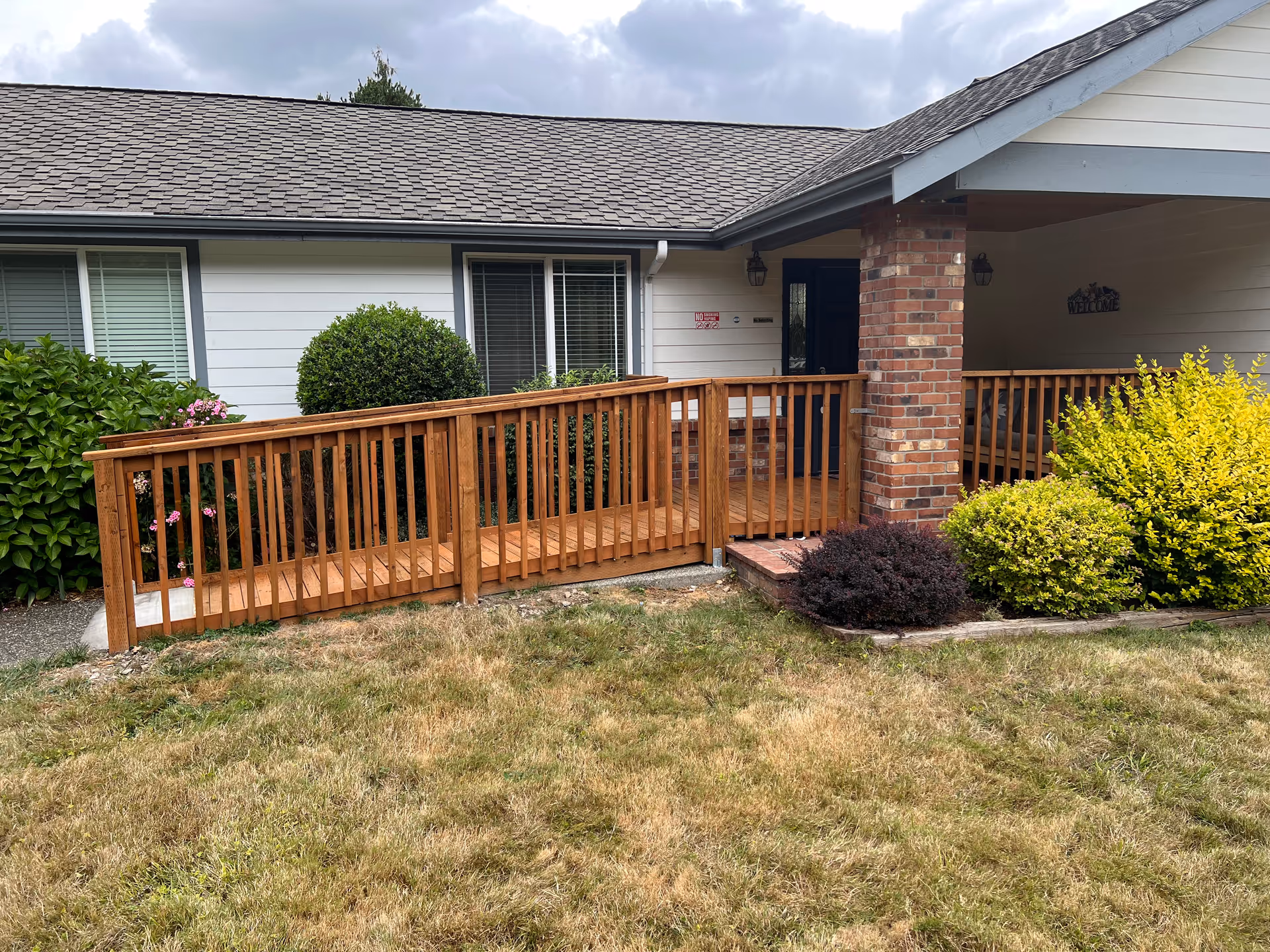 Single-story building with brick entrance, wooden ramp railing, and manicured shrubs in the front yard.