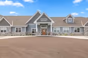Front exterior of a single-story grey residential building with a central covered entrance, stone accents, and a circular paved driveway.