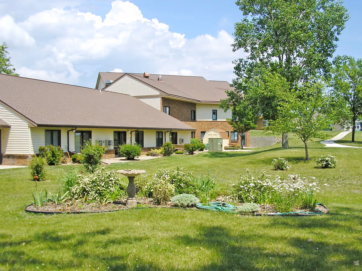 Front view of a senior living center with a manicured lawn and garden beds.