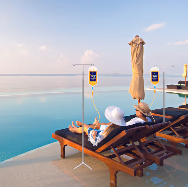 Two people relax on poolside lounge chairs by a calm blue infinity pool.