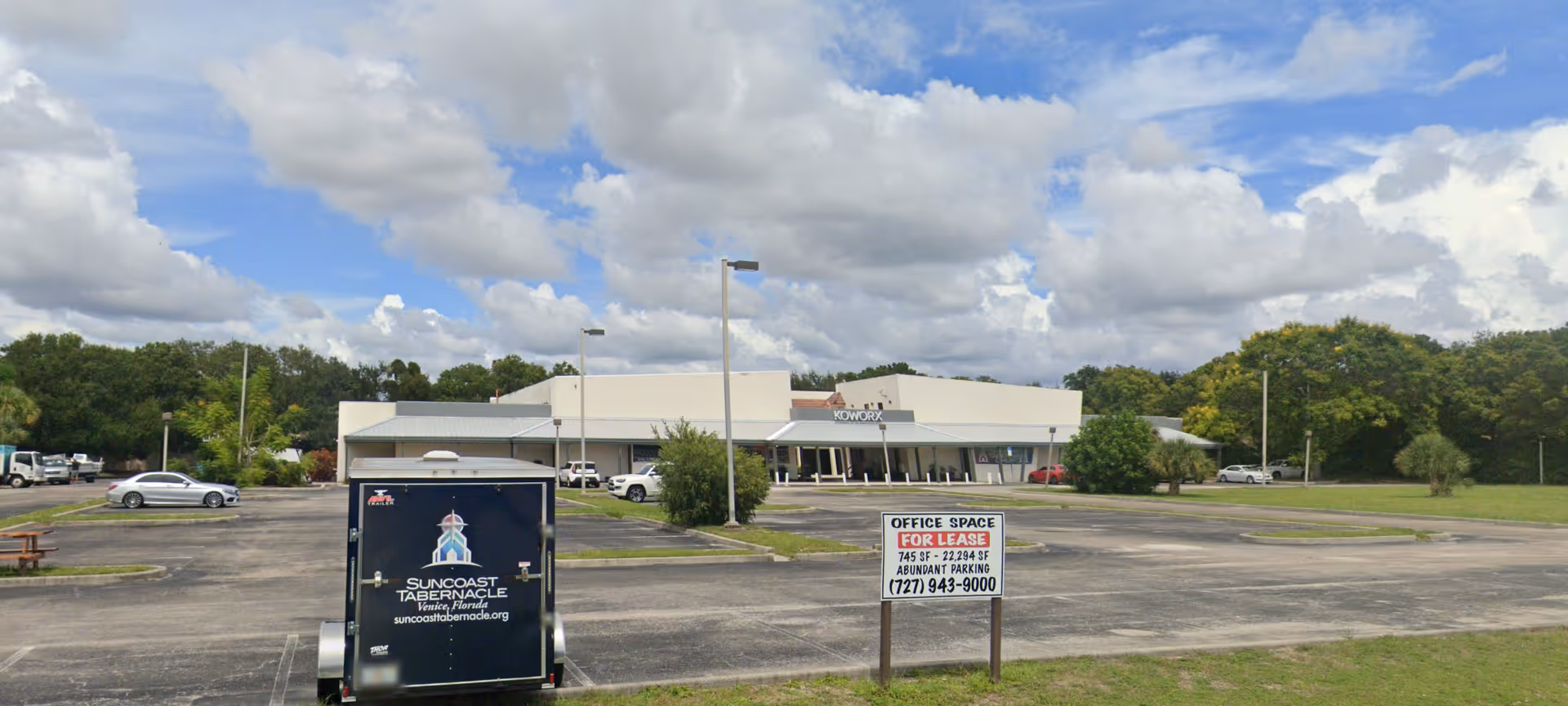 Exterior view of a single-story building with a large parking lot and front sign.