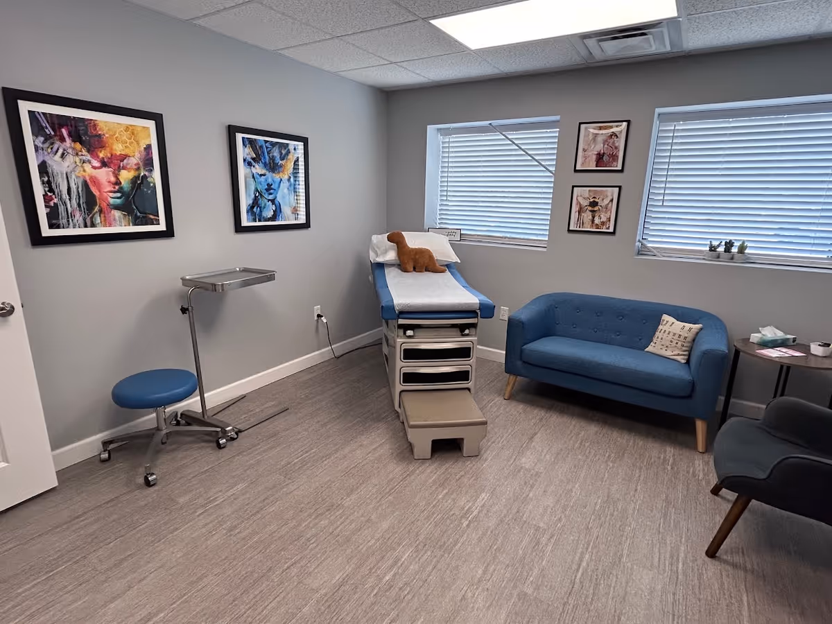 A compact clinic room with an examination table, blue seating, and wall art.