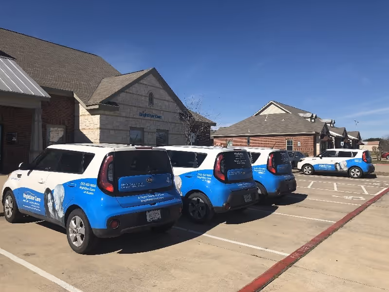 BrightStar Care branded vehicles park in a lot outside a senior facility under a clear sky.