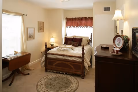 A cozy senior living bedroom with a four-poster bed, dresser, and bedside lamps.