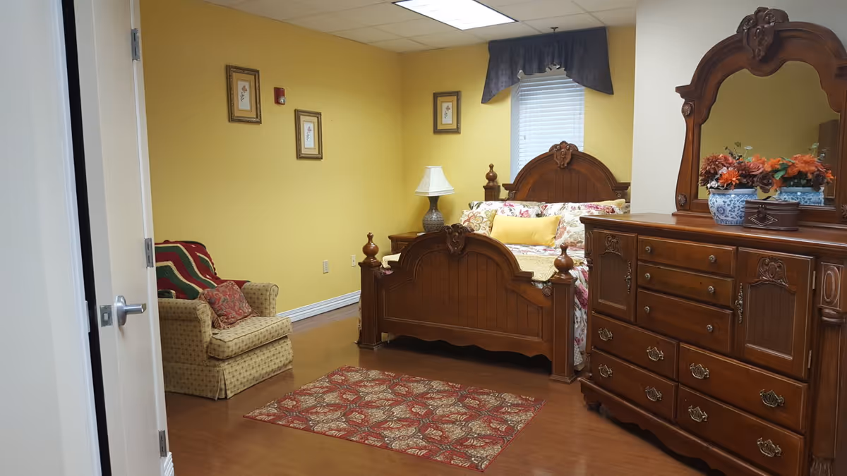 A furnished bedroom featuring a wooden bed, dresser, lamp, and floral bedding in yellow walls.