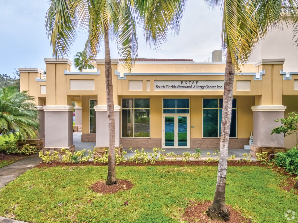 Exterior view of a beige medical building with palm trees and glass entrance
