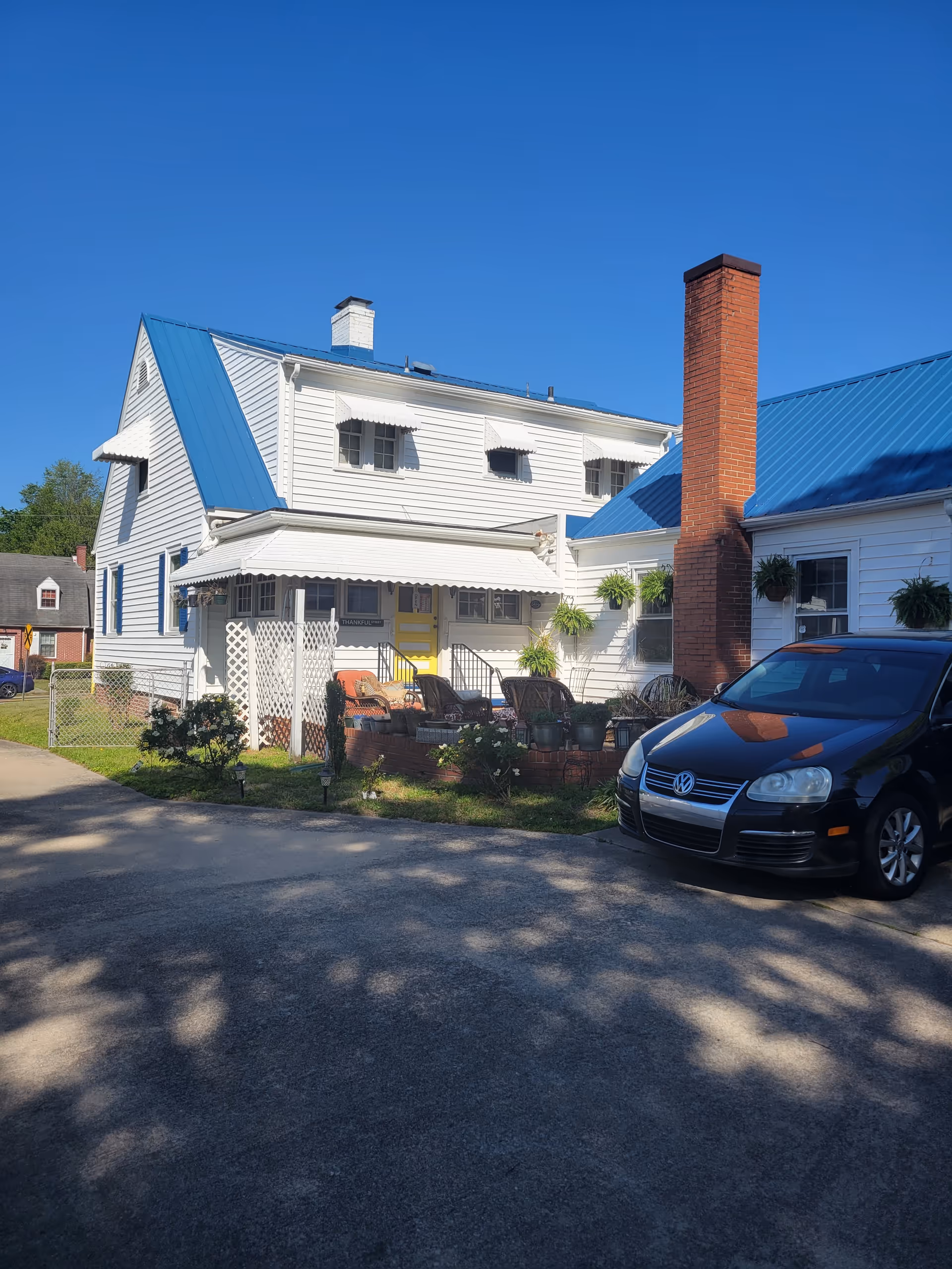 Front exterior of a senior living facility: white house, blue roof, brick chimney, patio seating.