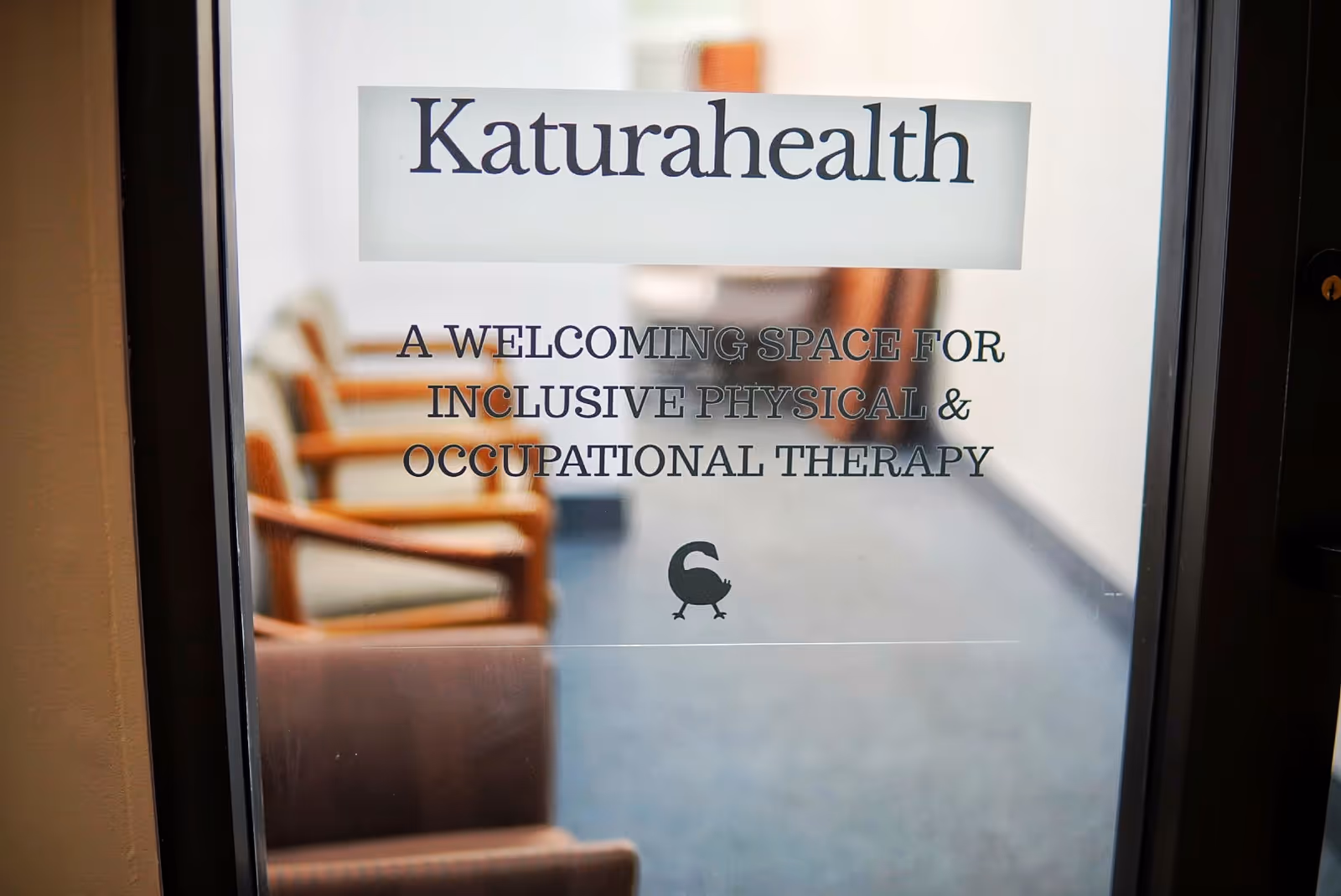 Interior doorway displays KaturaHealth sign with waiting chairs in hallway.