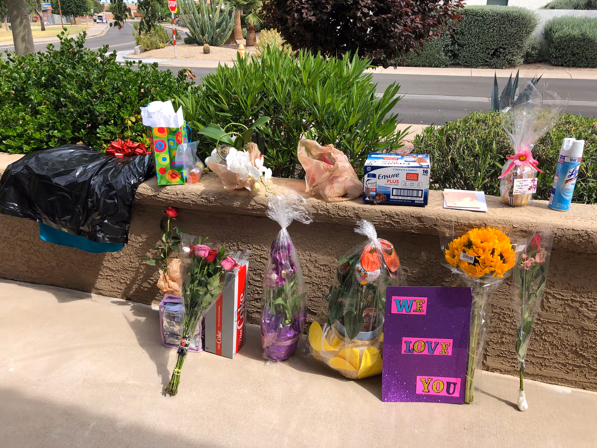 Outdoor walkway with gifts and flowers arranged along a low brick wall.