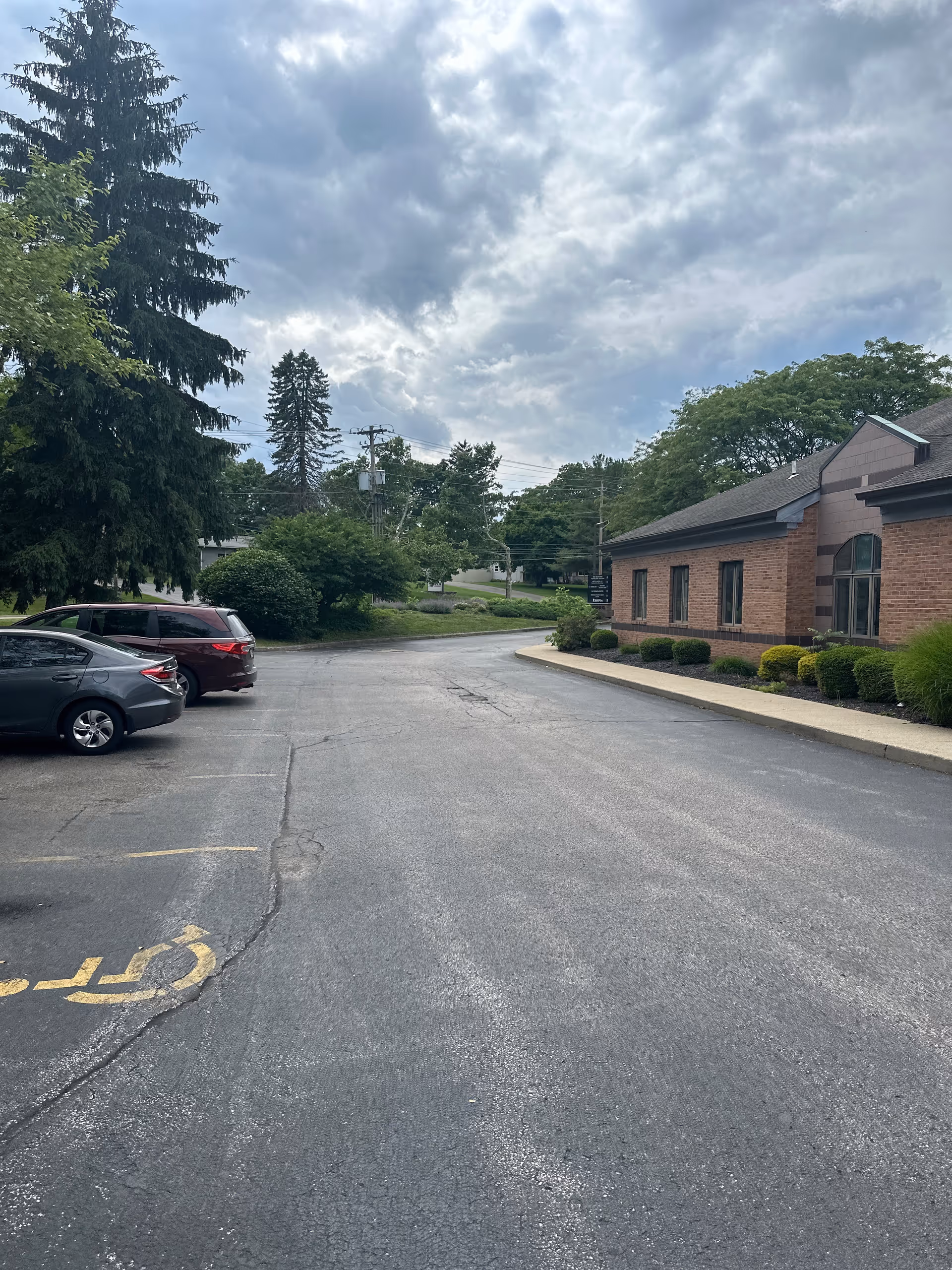 Exterior view of a brick senior living facility with a parking lot and trees.