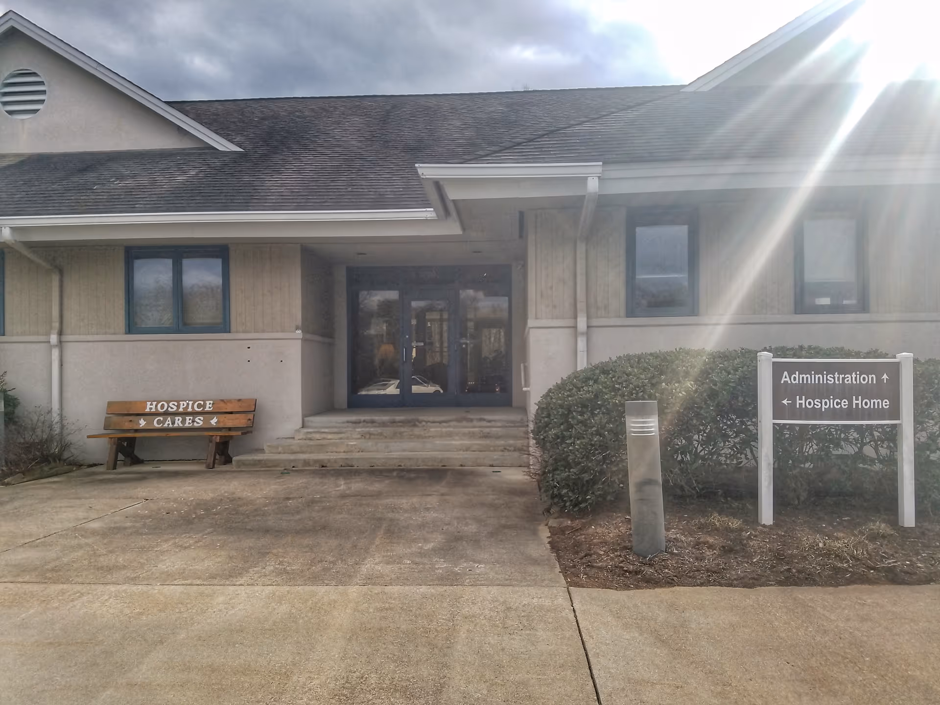 Exterior view of Ancora Compassionate Care entrance with hospice signs and a wooden bench.