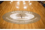 Circular White Oaks logo on a polished wooden floor in a facility hallway.
