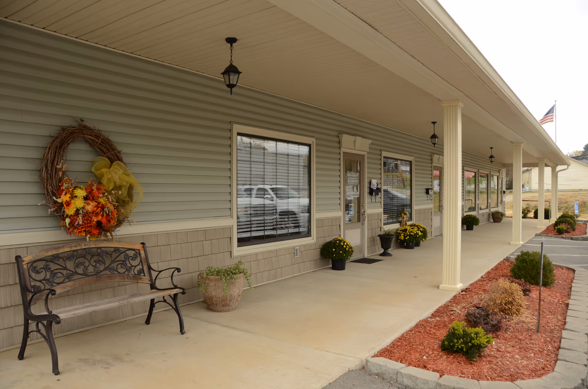 Exterior view of a senior living facility entrance with bench, wreath, and planters along the walkway.