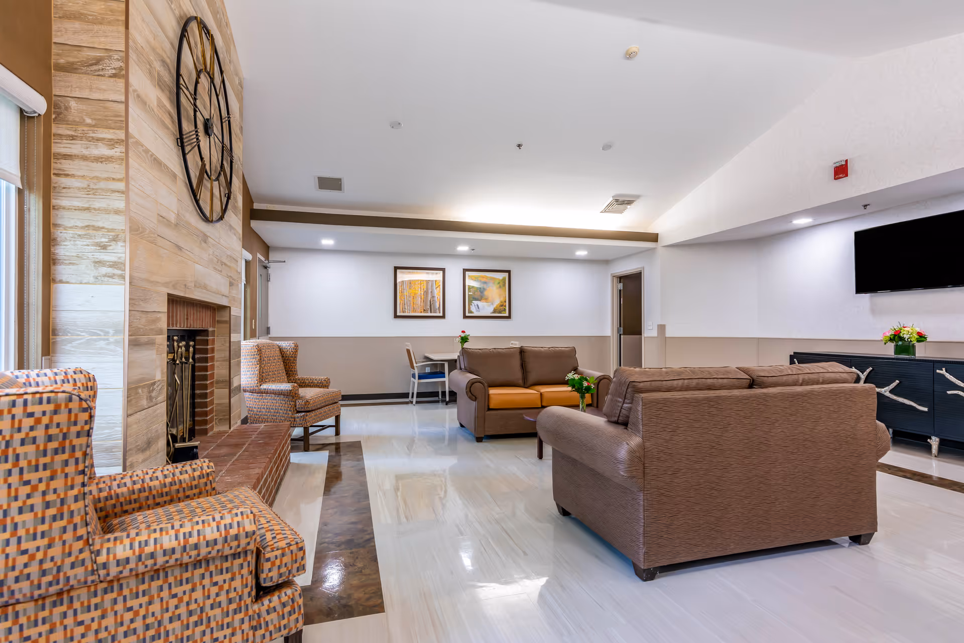 Spacious lounge area with brown sofas, a fireplace, and a wall clock.