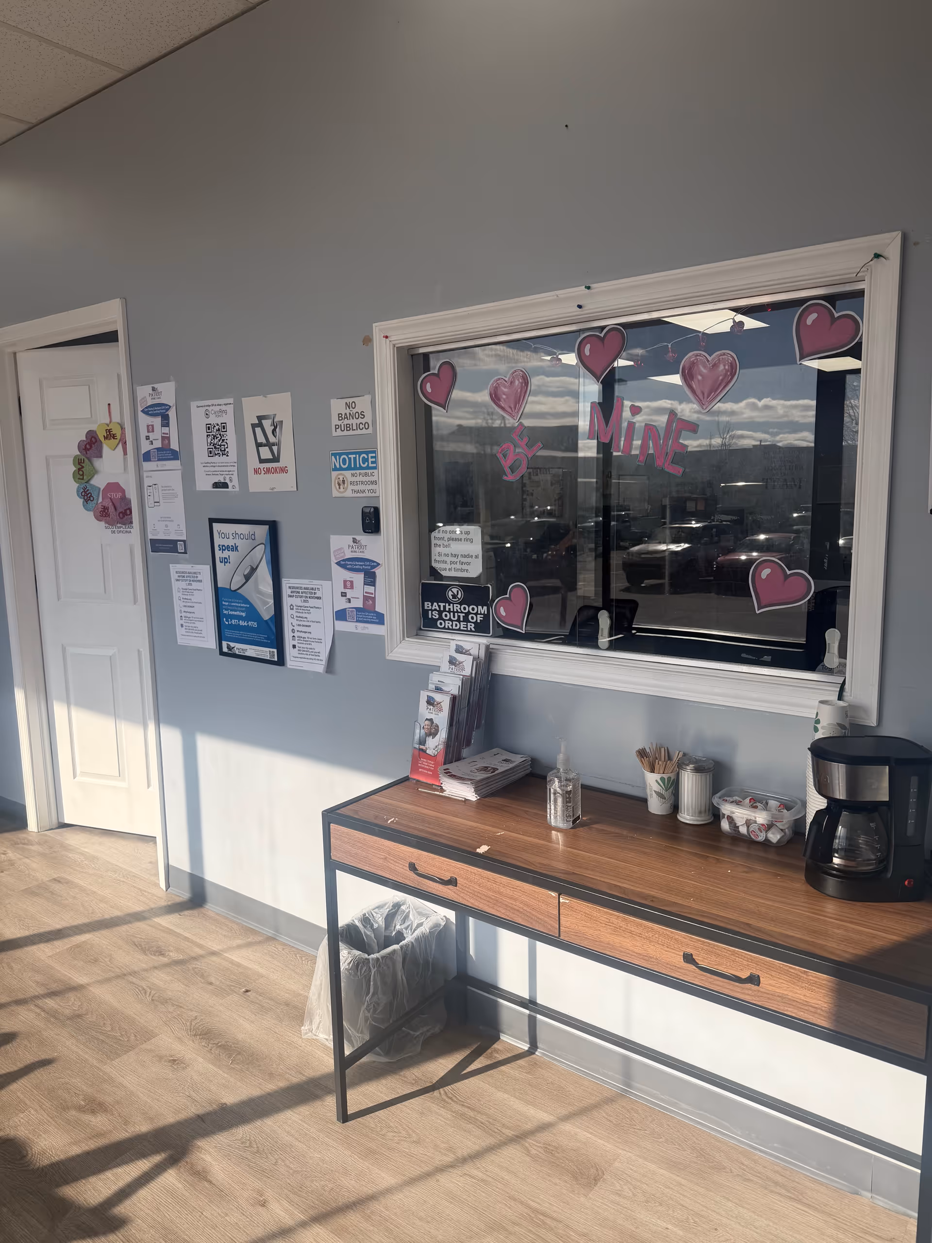 Interior hallway with bulletin board, coffee station, and window decorated with pink hearts.