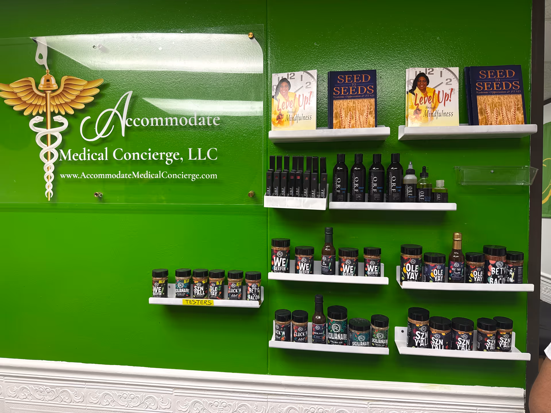 Bright green wall with Accommodate Medical Concierge, LLC logo and shelves of bottled products.