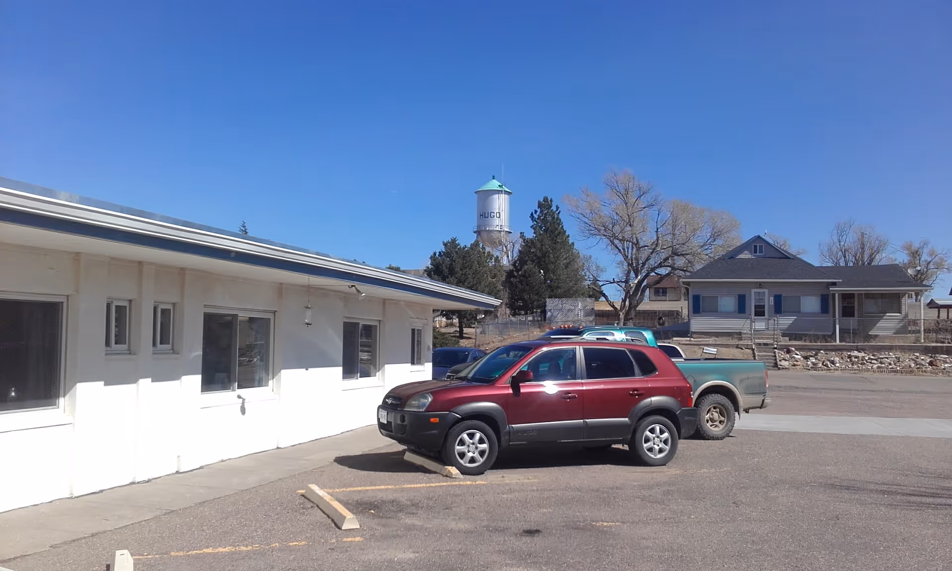 A single-story white facility with a parking lot and a red SUV in front.