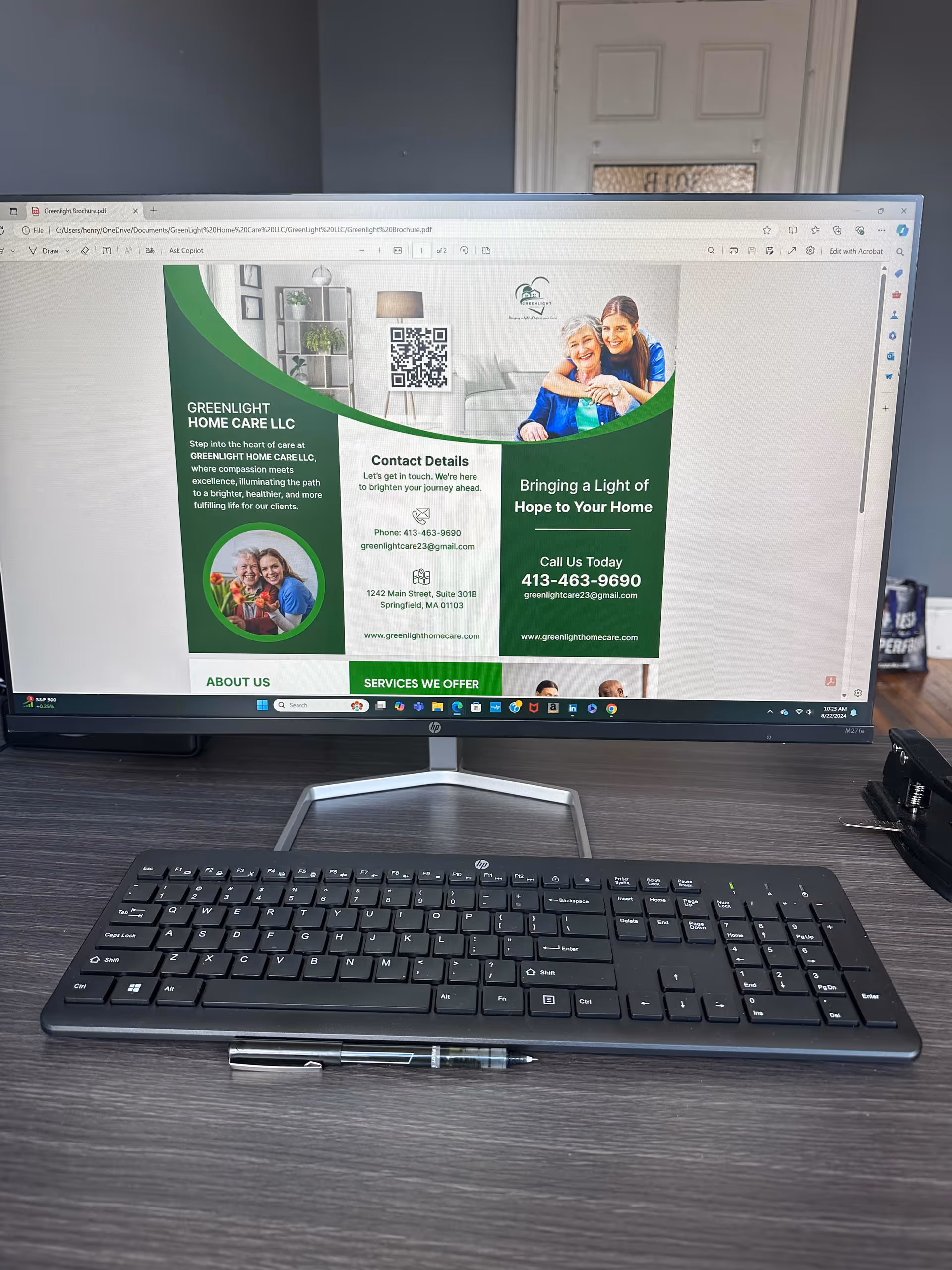 Monitor displays Greenlight Home Care LLC brochure on a dark wood desk with keyboard and pen.