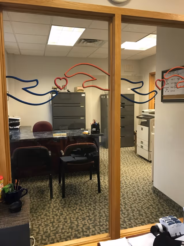 Glass-walled office area with desks, filing cabinets, and a copier inside a senior facility.