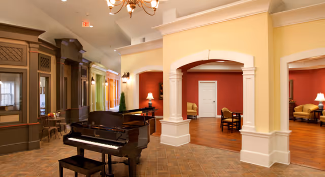 Bright communal lounge with a grand piano, arched columns, and several seating areas.
