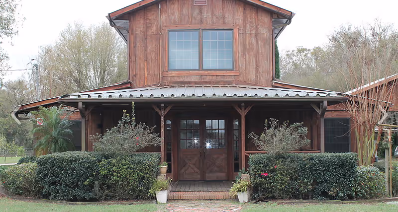 Rustic wooden building entrance with hedges and potted plants.
