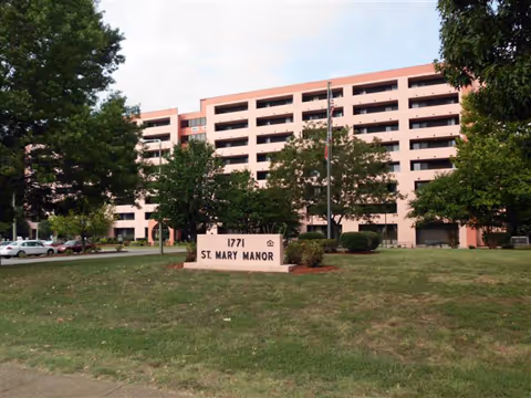 Pink multi-story senior living building with lawn, trees, and a St. Mary Manor sign.